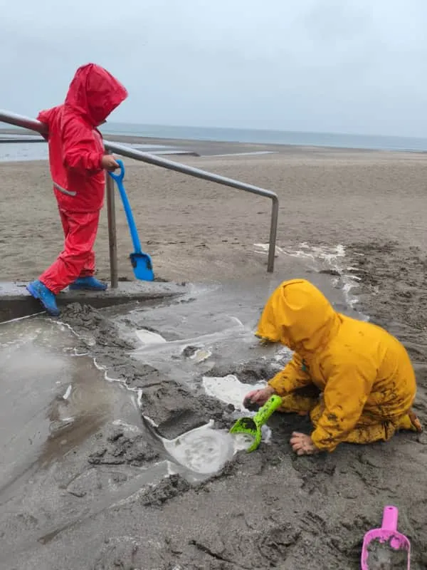 Children in rain gear digging at the beach